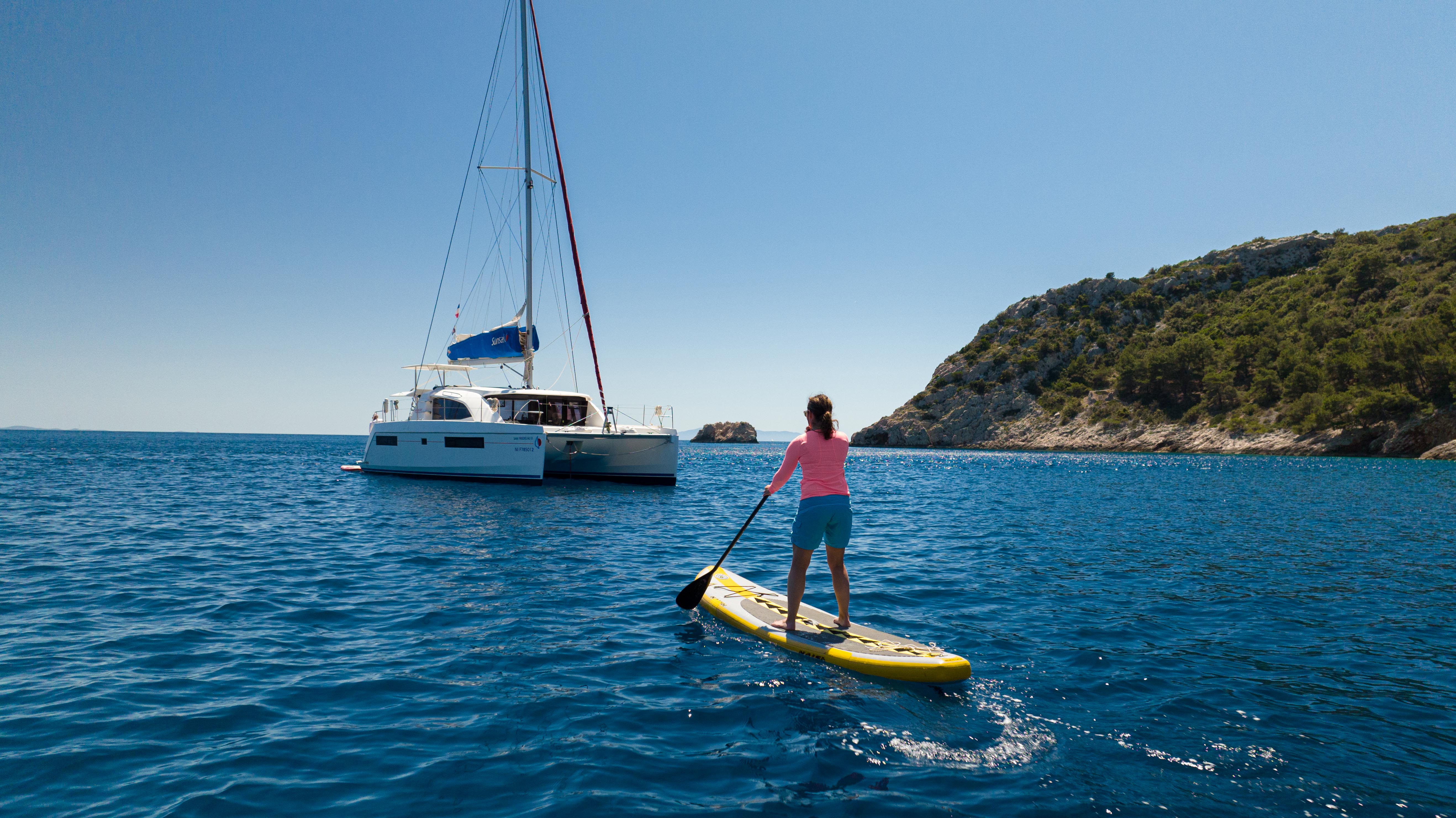 girl on paddle board next to sail catamaran yacht